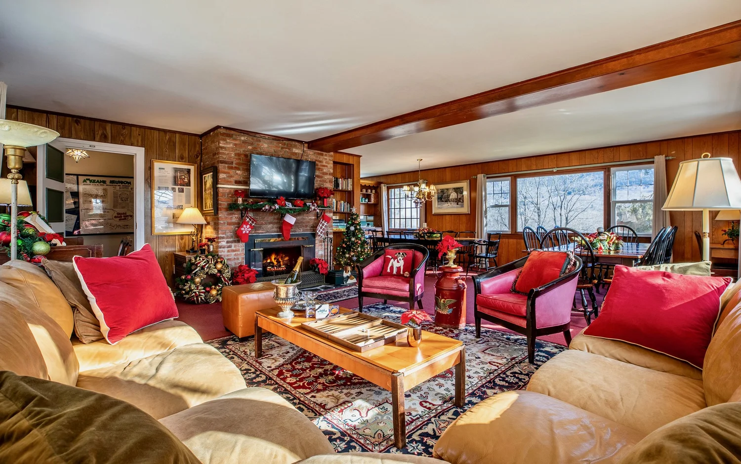 Cozy living room with festive decorations, a fireplace, comfortable seating, and a dining area visible through large windows.