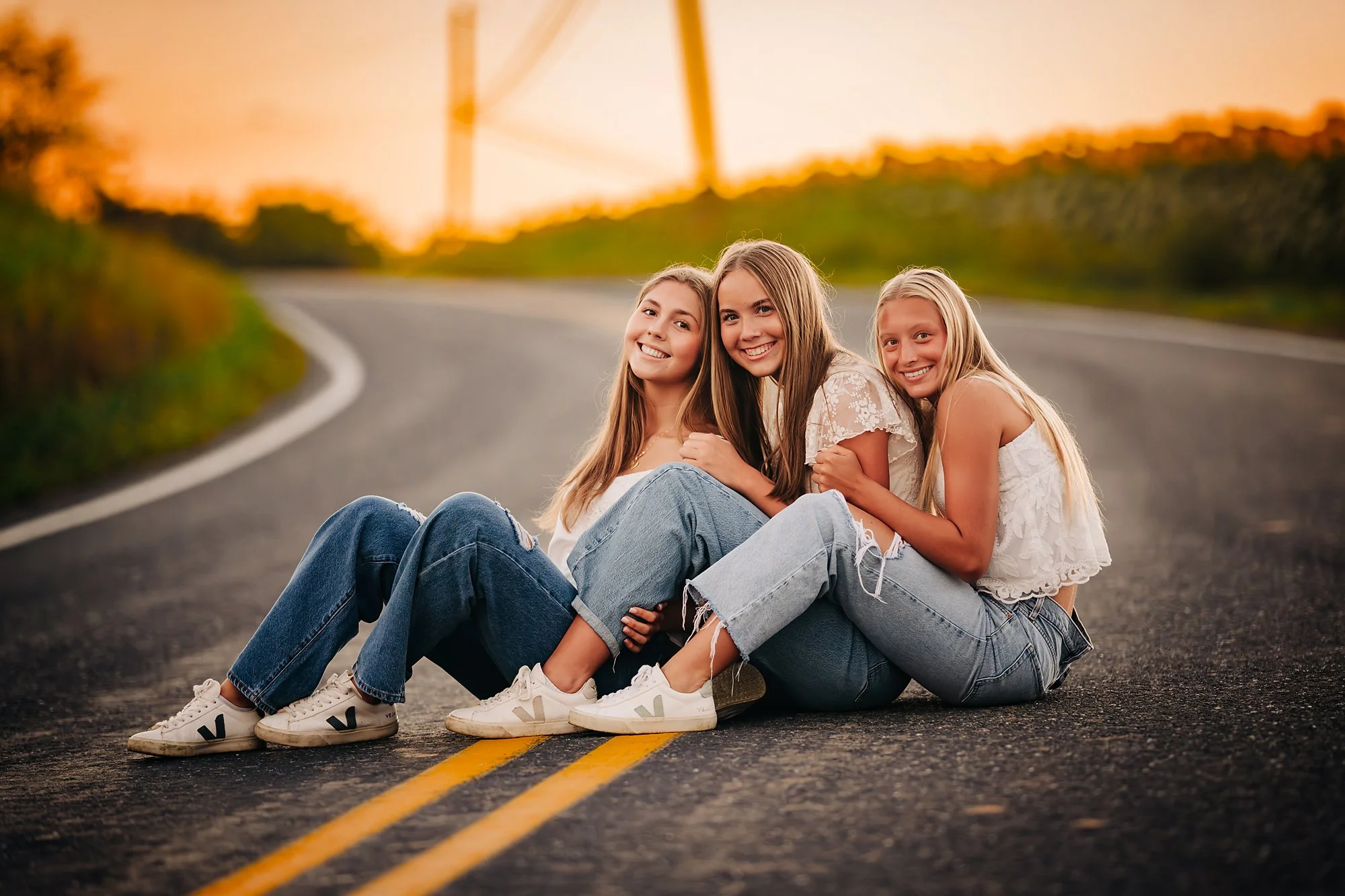 Three friends sitting together on a country road at sunset after a Lehigh Valley senior photo session.