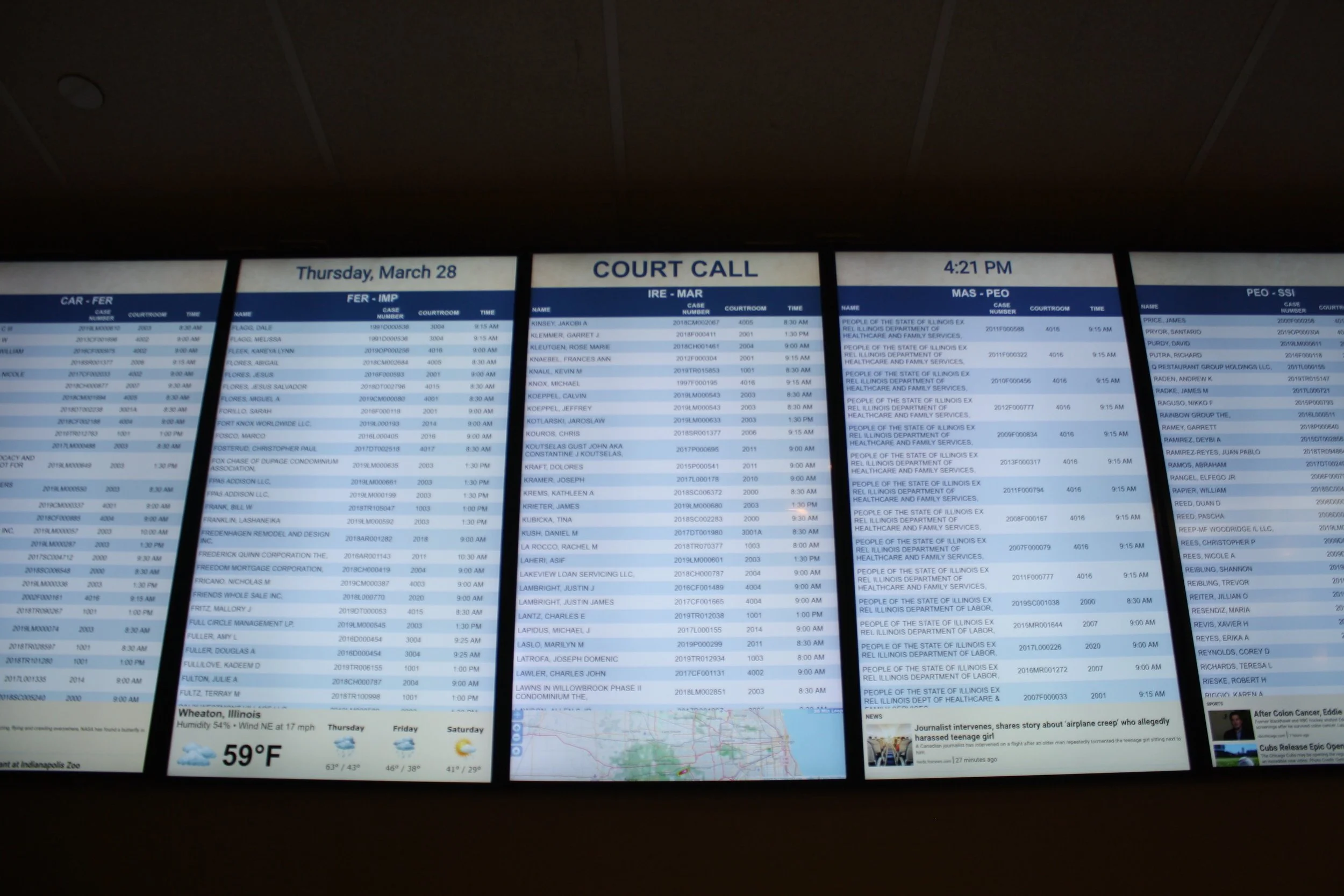 Large digital screens displaying court call schedules, weather forecast, and news at an courthouse.