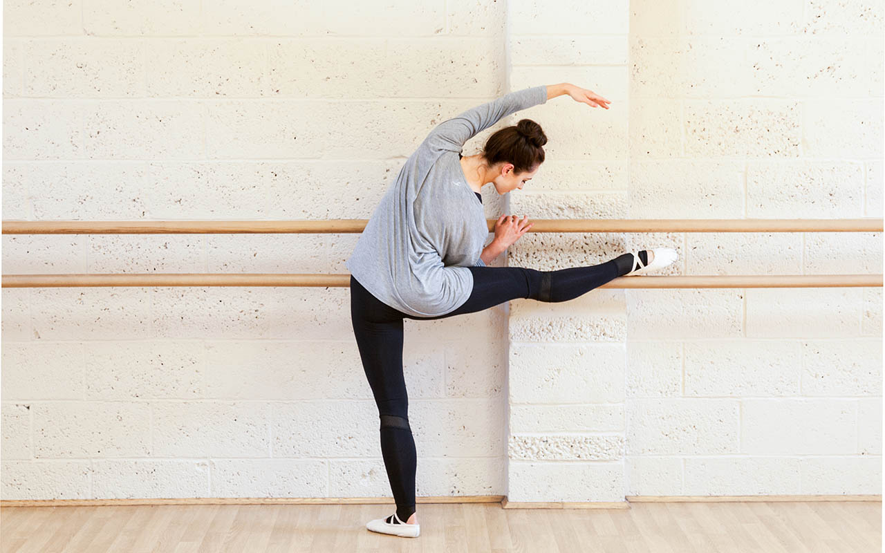 Daisy demonstrates at the barre, wearing the Zara Extended Mesh Legging and the Aubrey Knot Long Sleeve Tee from the Atelier Collection