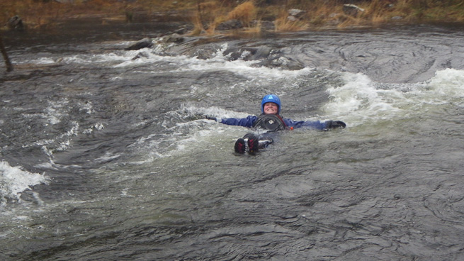 a person in a dry suit swimming with their feet up in whitewater
