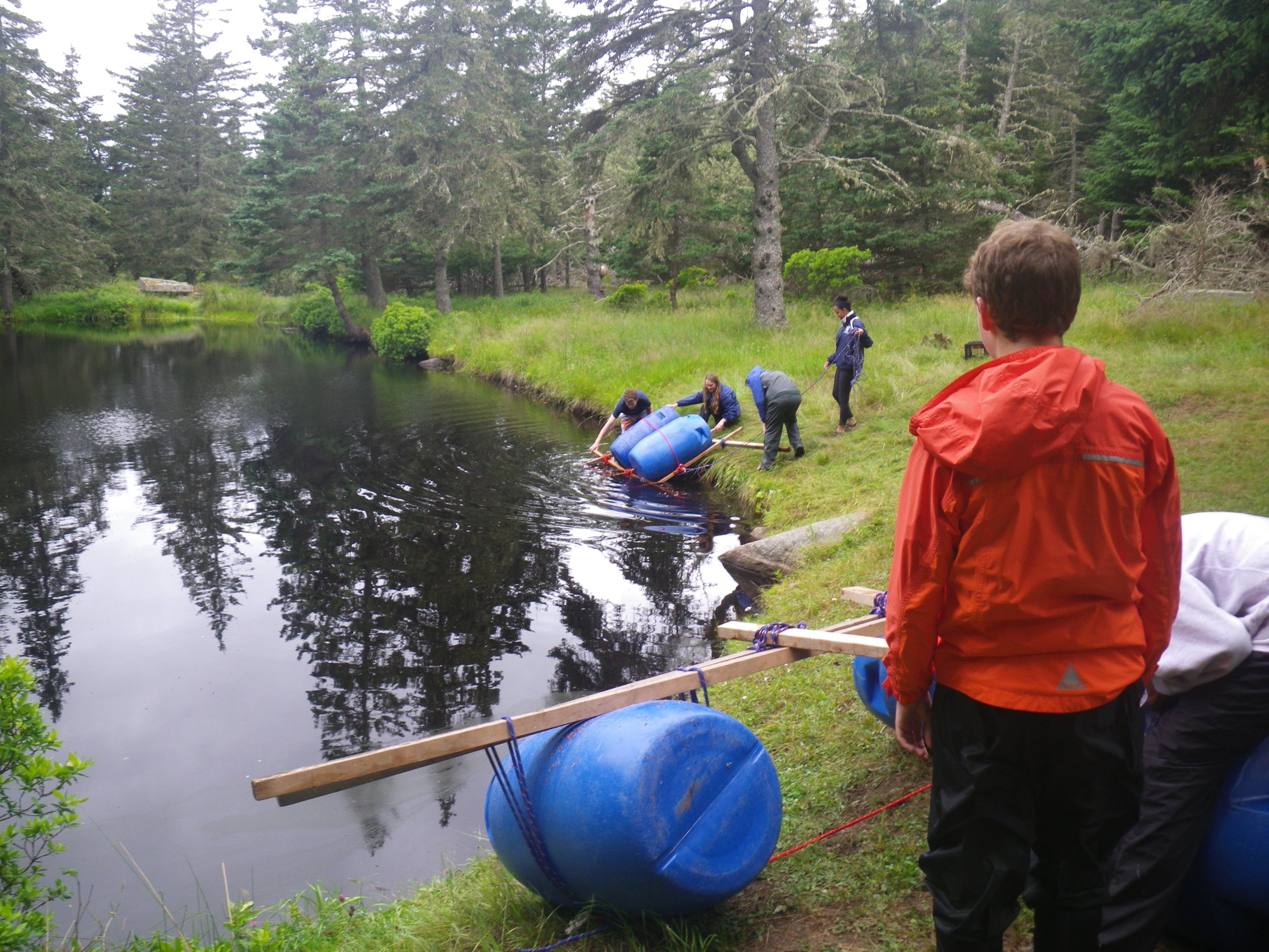 Students transition from the land to the water in teams during our rainy day raft challenge.