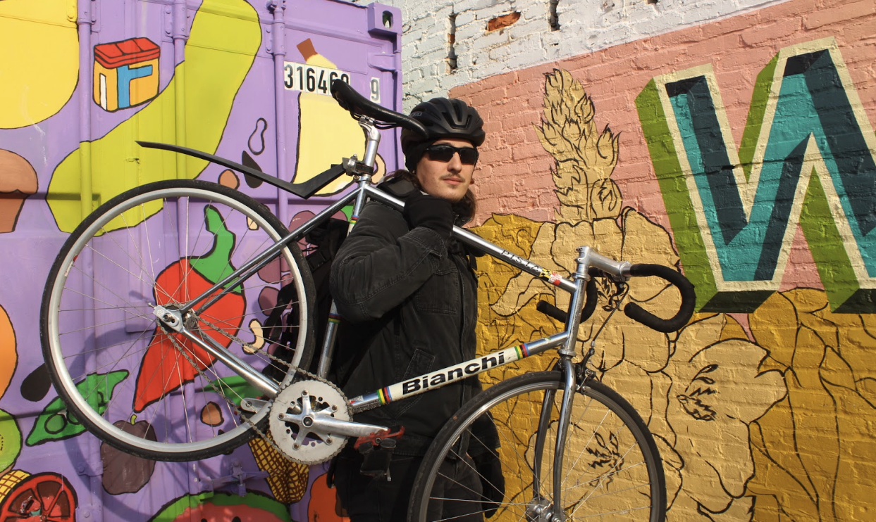 an image of Mike Thomas holding his bianchi bicycle in front of a shipping container at Waverly Farmers Market