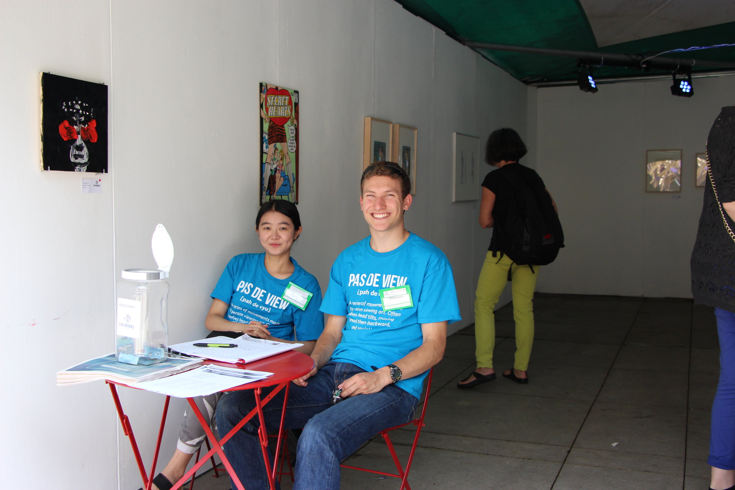 Two volunteers sitting in an art exhibit, The Best of the Cabinet of Queeriosities, 2016.