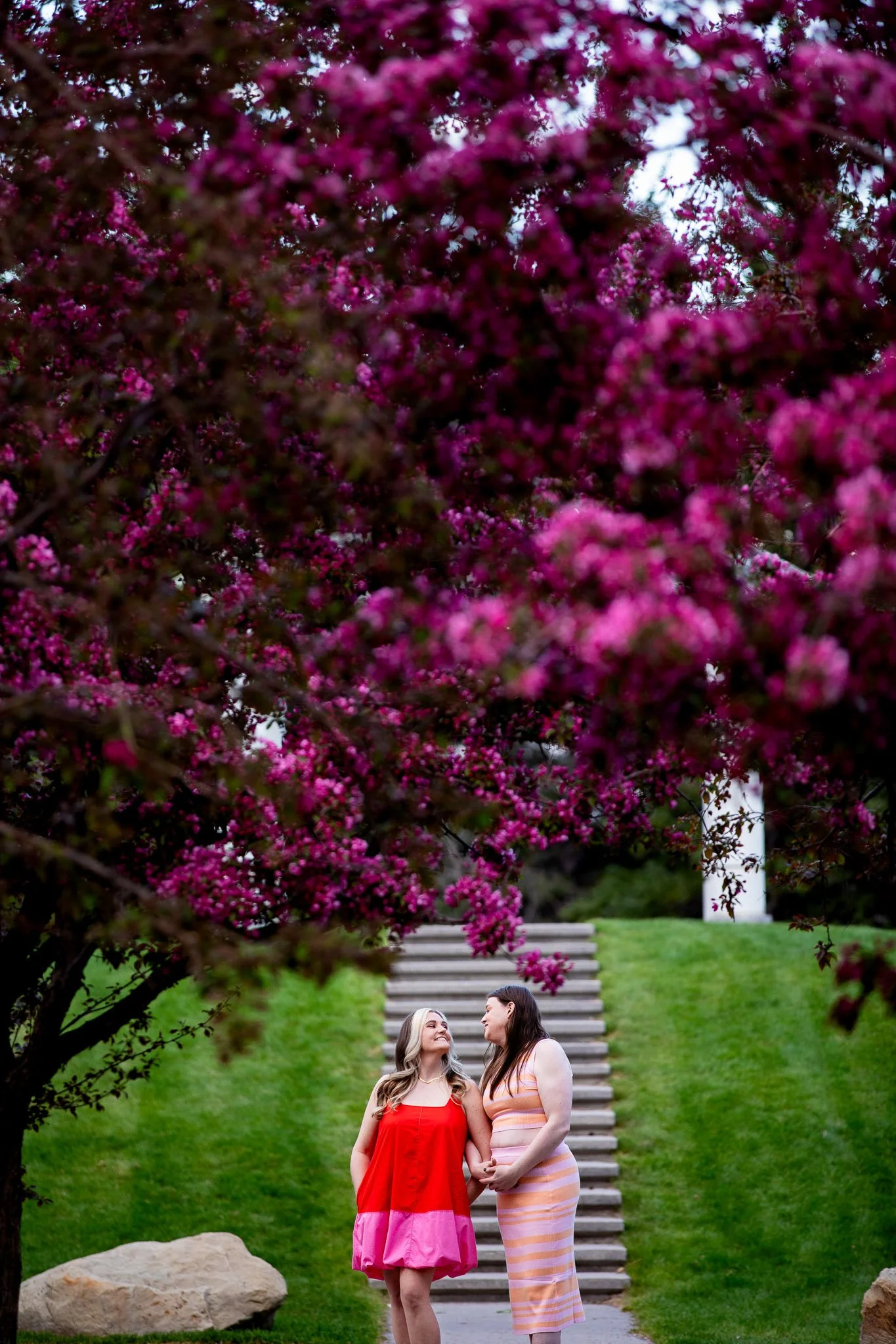 Couple walking hand in hand through blooming lilacs during a spring engagement session in Calgary.