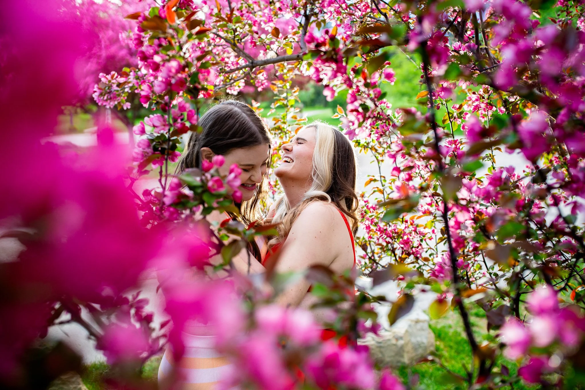 Couple laughing together while surrounded by pink spring flowers in Baker Park.