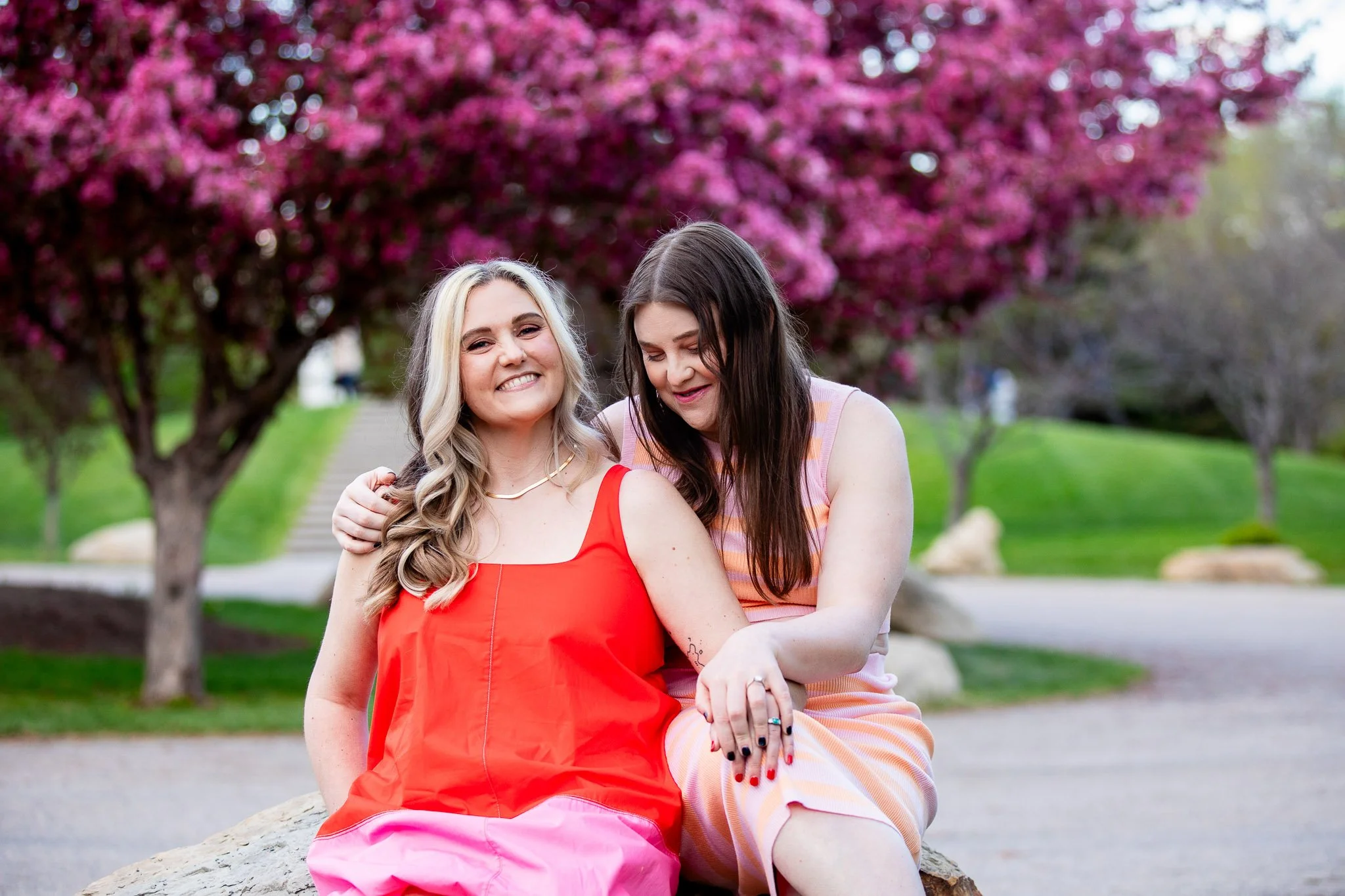 Dianna and Annika standing beneath blooming spring trees during an evening engagement session at Baker Park.