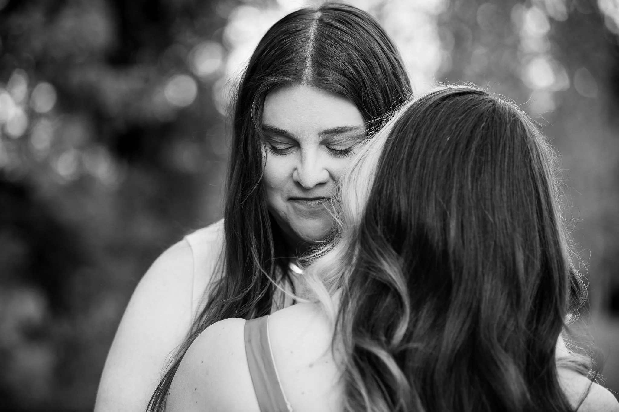 Close-up portrait of Dianna and Annika sharing a tender moment among flowering trees in Baker Park