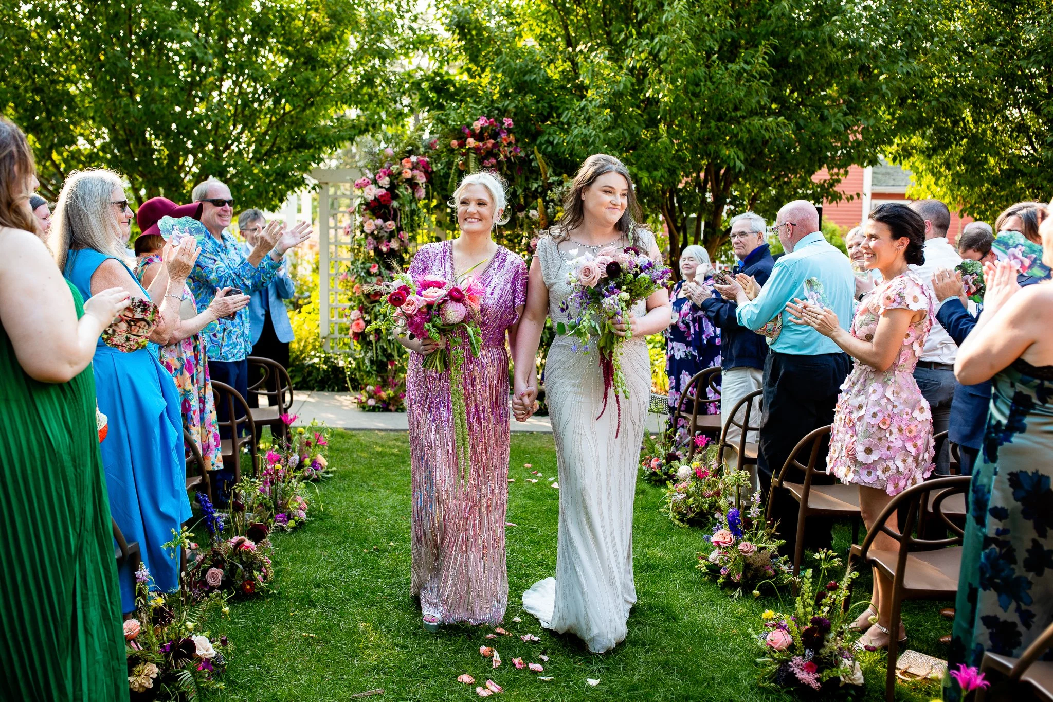 A couple celebrates their love in front of large floral arch at their garden wedding at The Deane House in Calgary, Alberta.