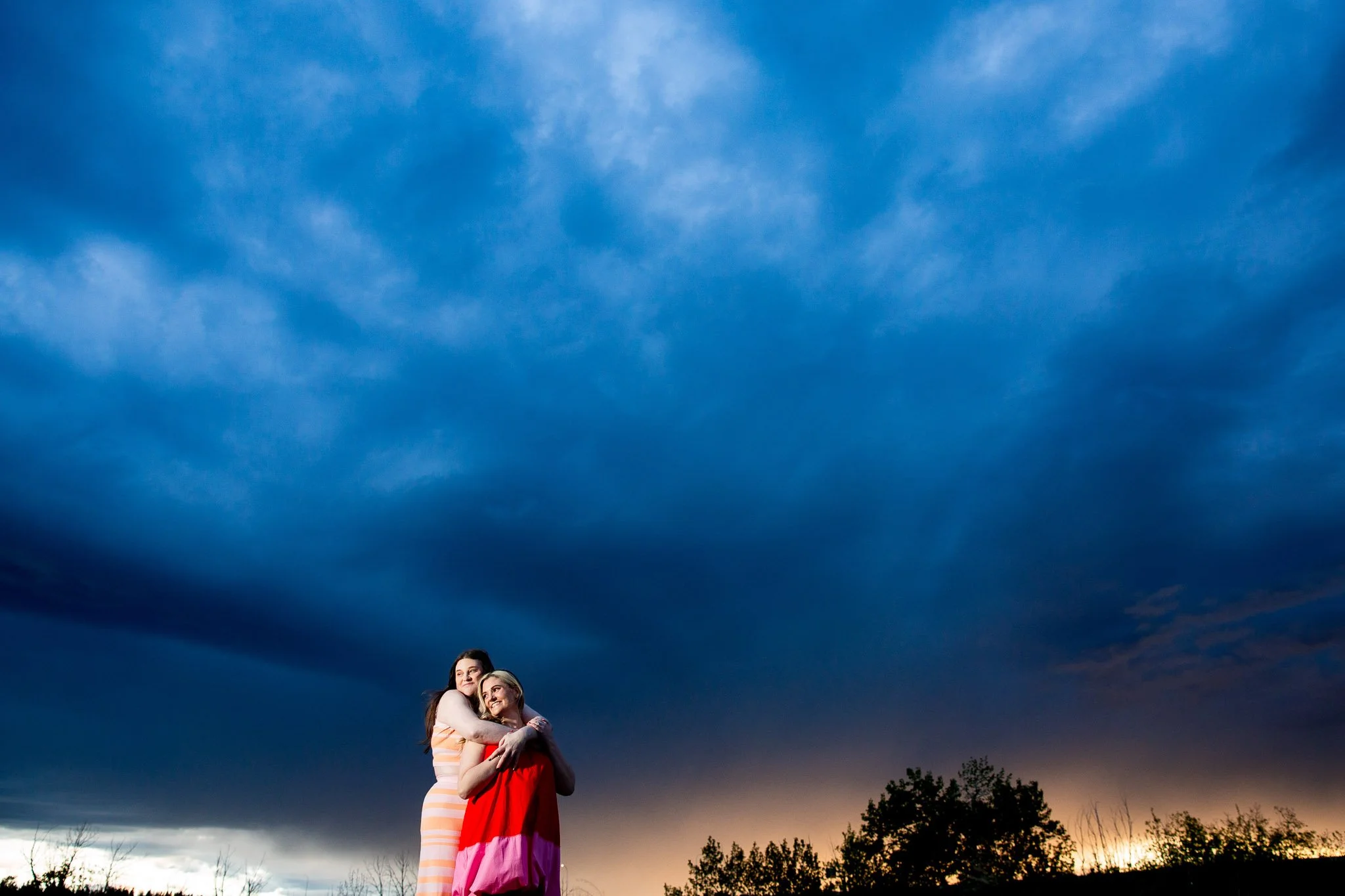 wide image of couple embracing with dark blue sunset behind them
