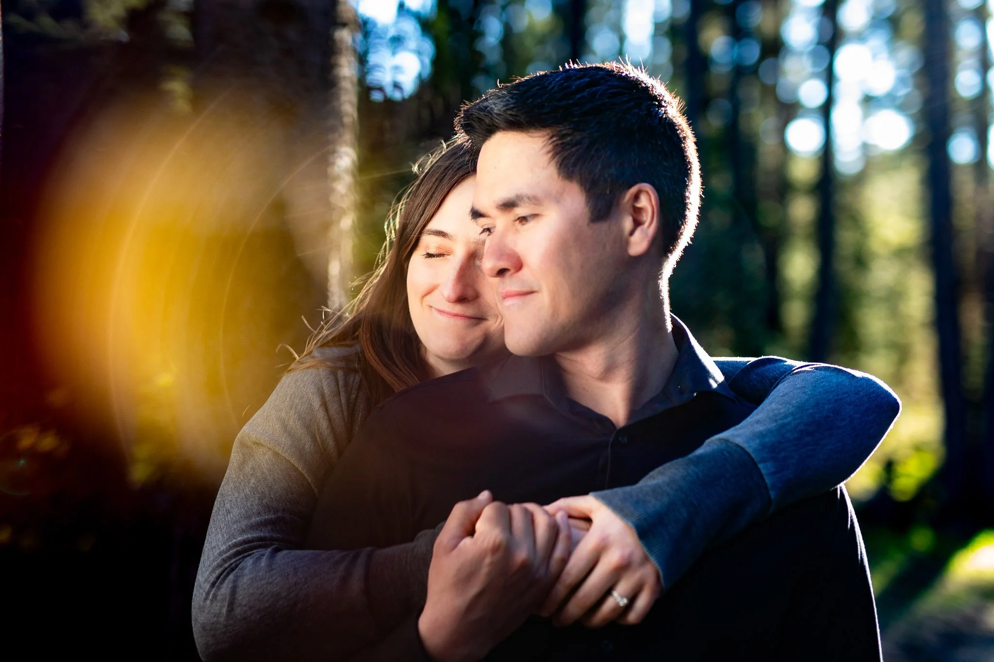 Megan and Robert during their engagement session at Shannon Terrace in Fish Creek Park, Calgary, surrounded by evergreen trees and golden evening light