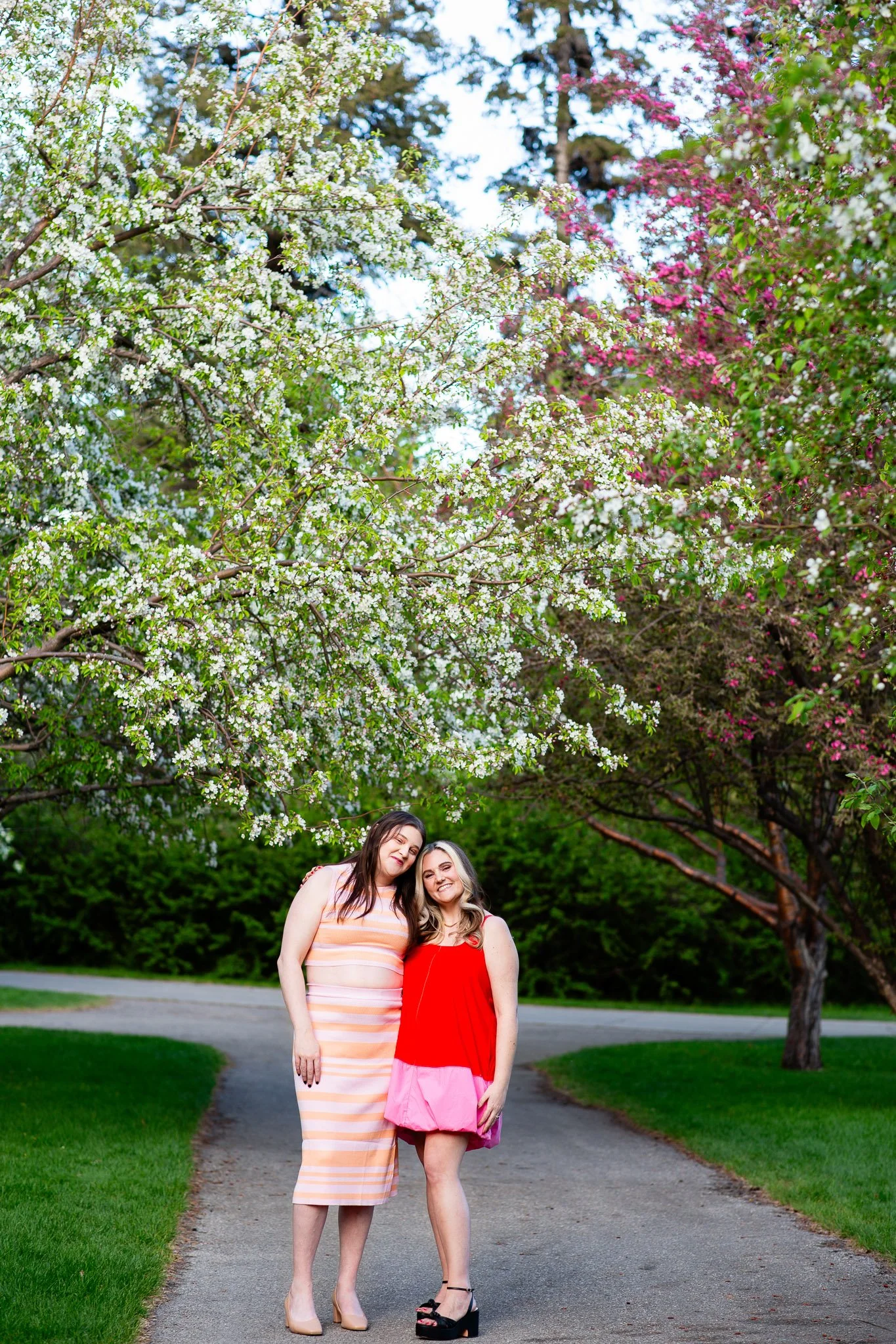 Dianna and Annika strolling along a flower-lined pathway near the Bow River during their spring engagement session.