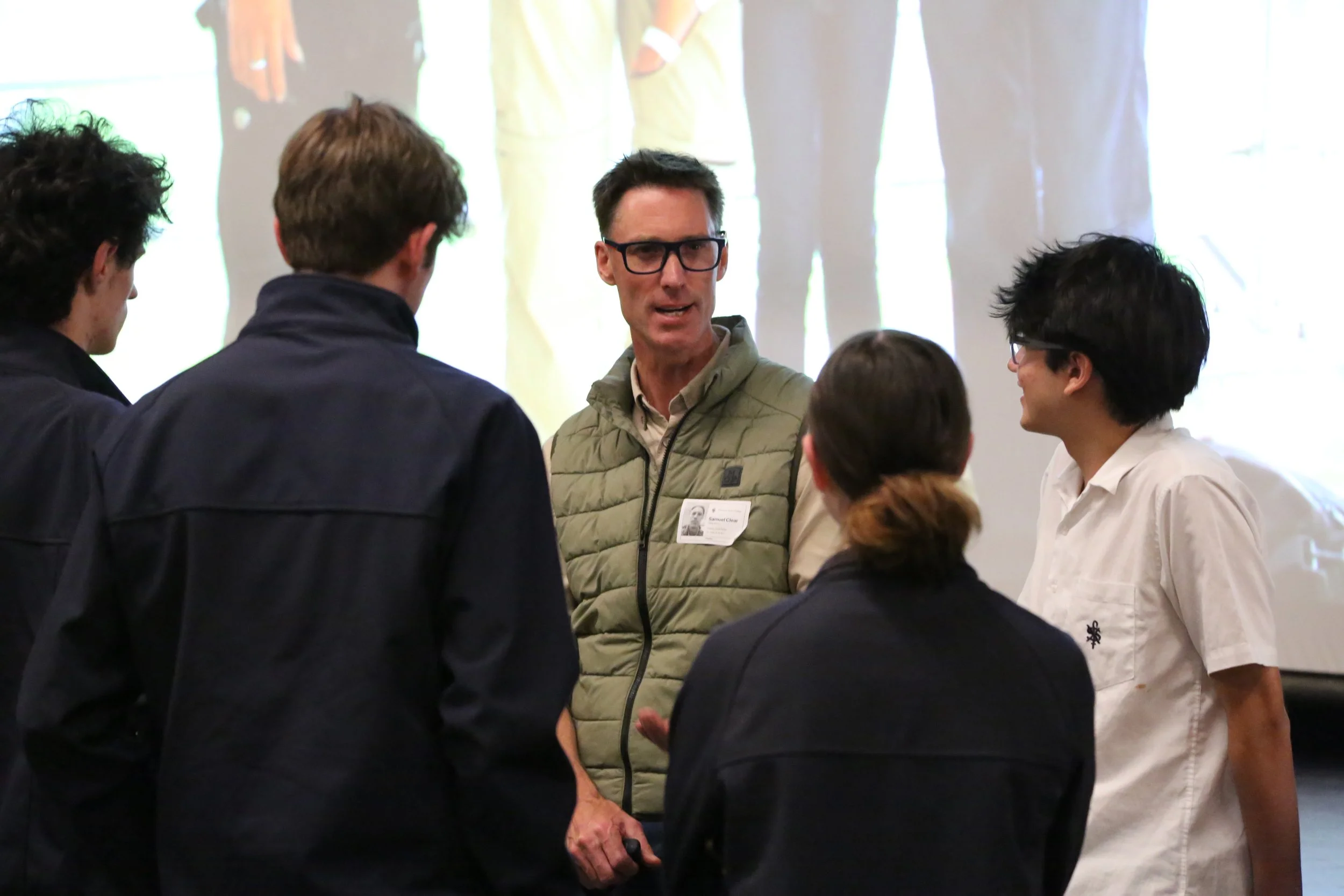 Sam Clear with a group of four people having a discussion on a reflection day, with a presentation or screen in the background.