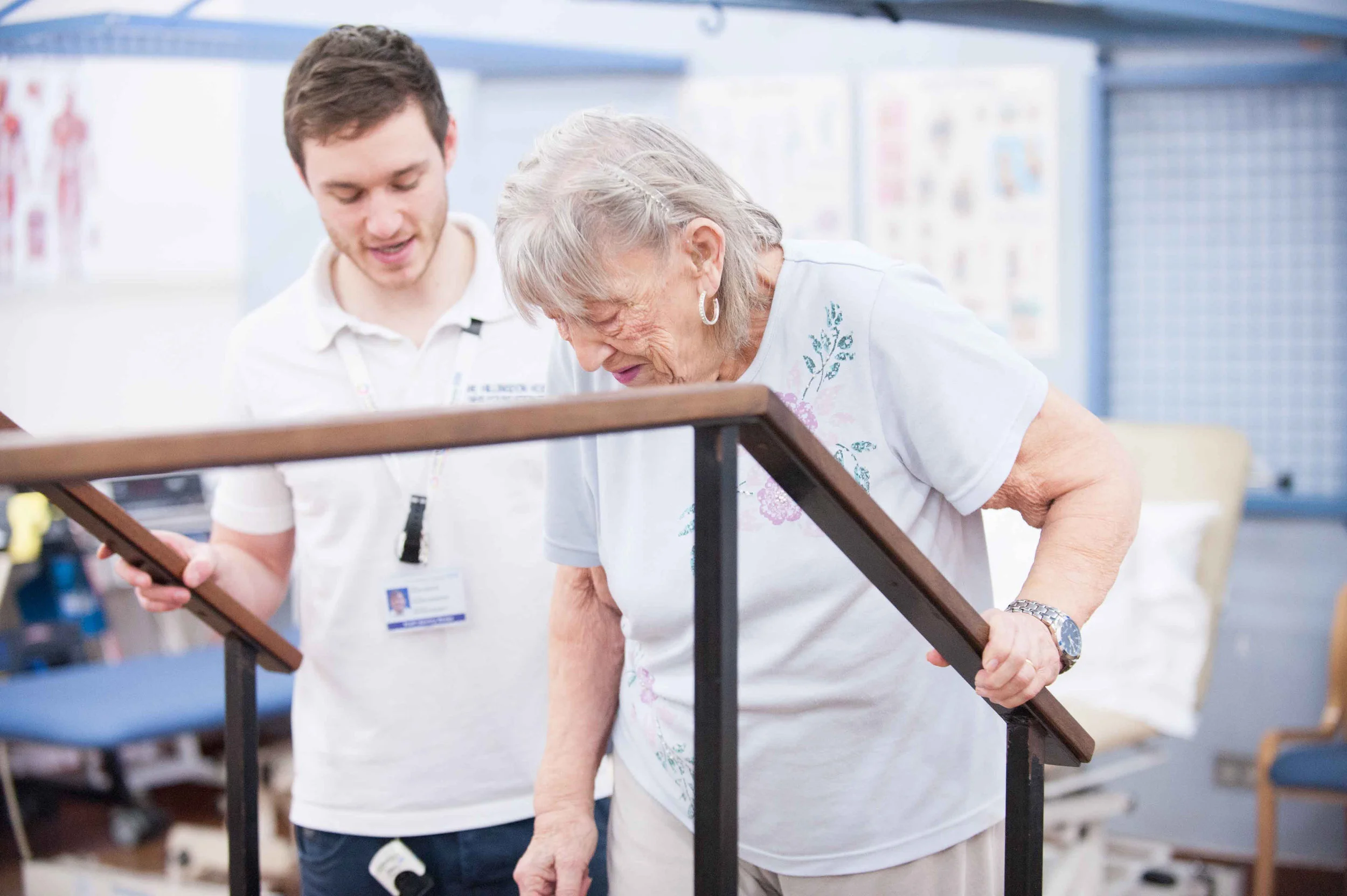 A physiotherapist helps and elderly woman to walk using walking bars in Hospital