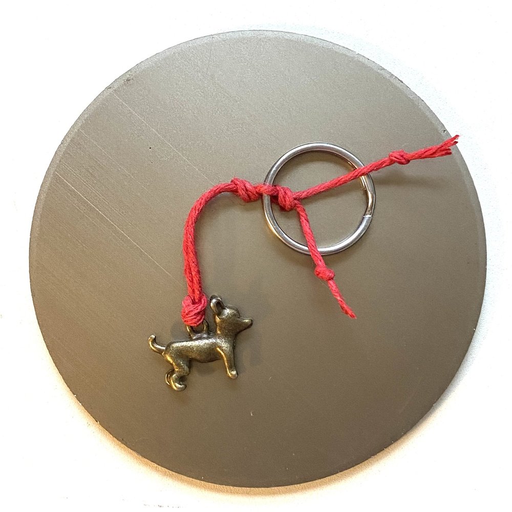 A small metal Chihuahua charm tied to a keychain with a red string