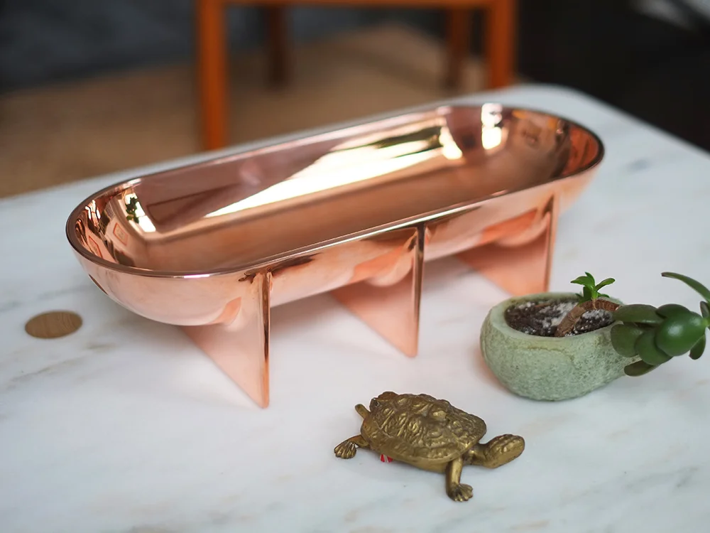 Large Copper Standing Bowl styled on a white marble coffee table with brass accessories