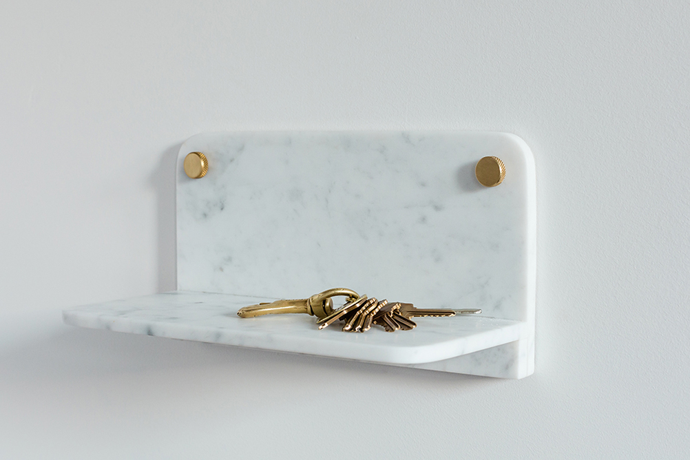 White Carrara Marble Stone Shelf holding brass keys on a white background