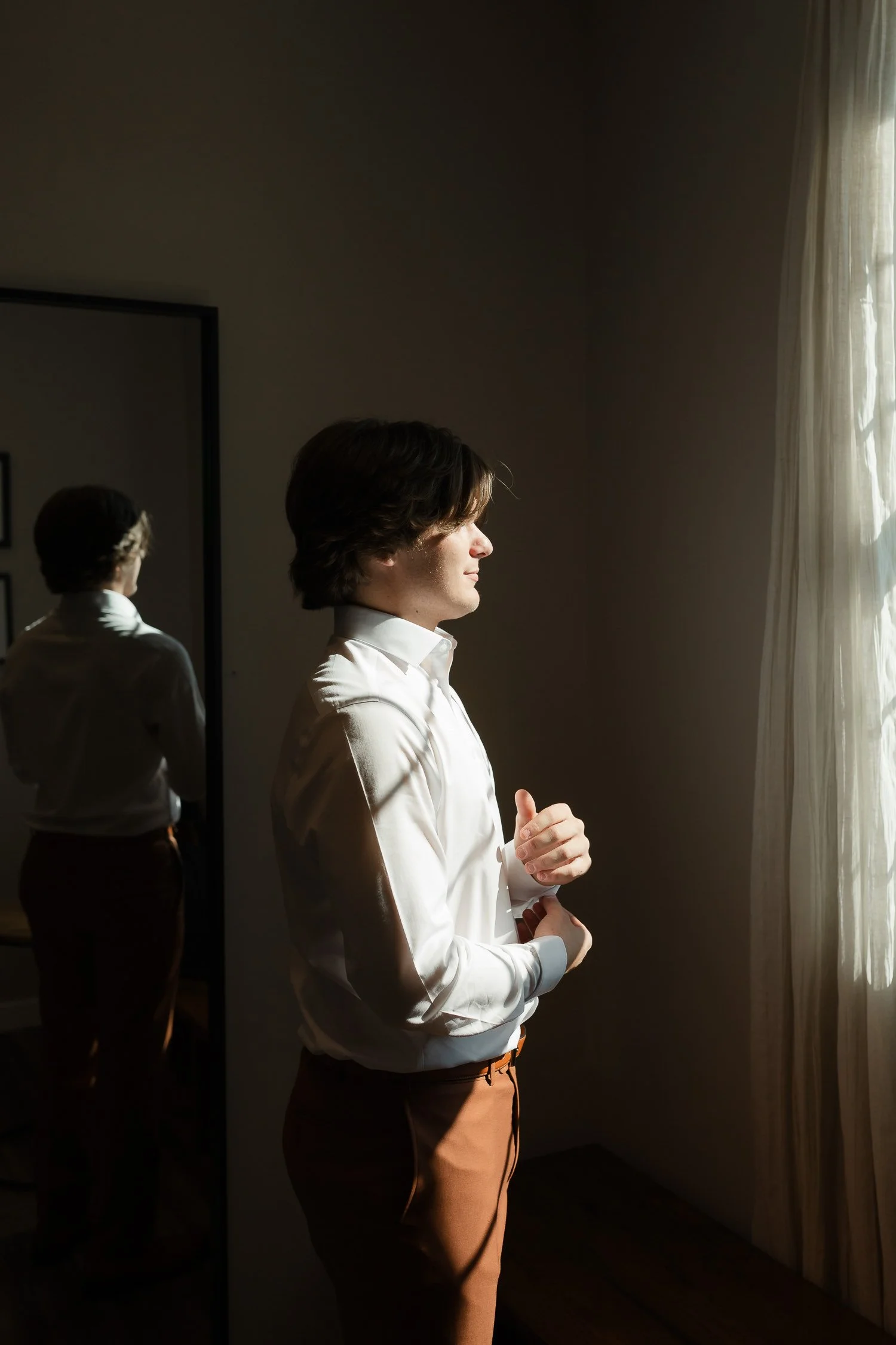 Groom getting ready by a window in natural light during an Ivory Meadows wedding in Yellow Springs, Ohio.