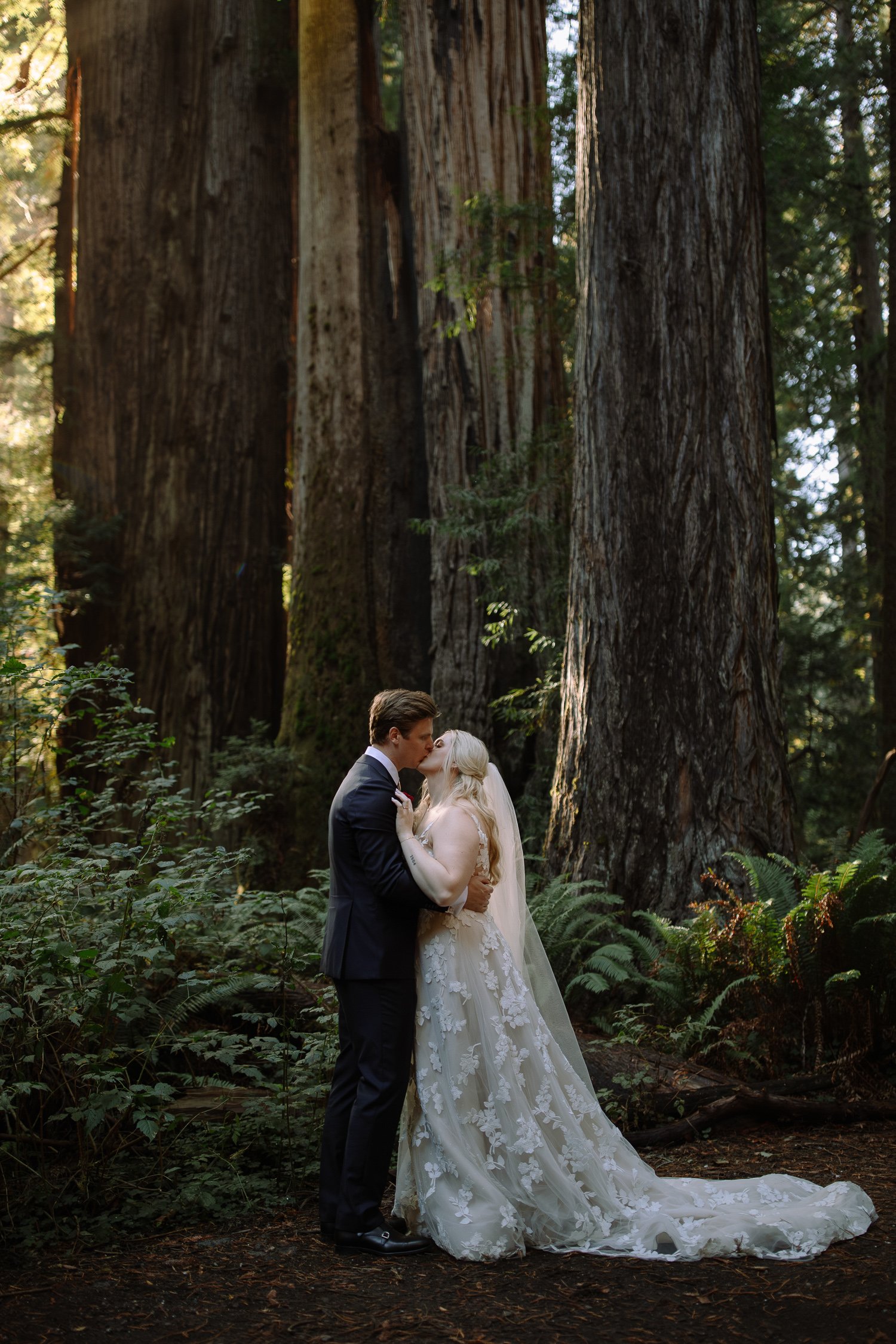 Bride and groom kissing beneath towering redwood trees in Prairie Creek Redwoods State Park
