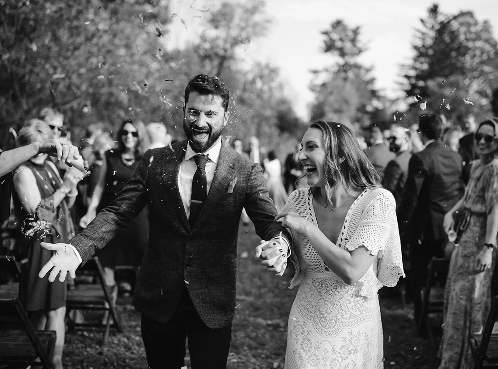 Bride and groom laughing as guests throw confetti during their outdoor wedding ceremony exit