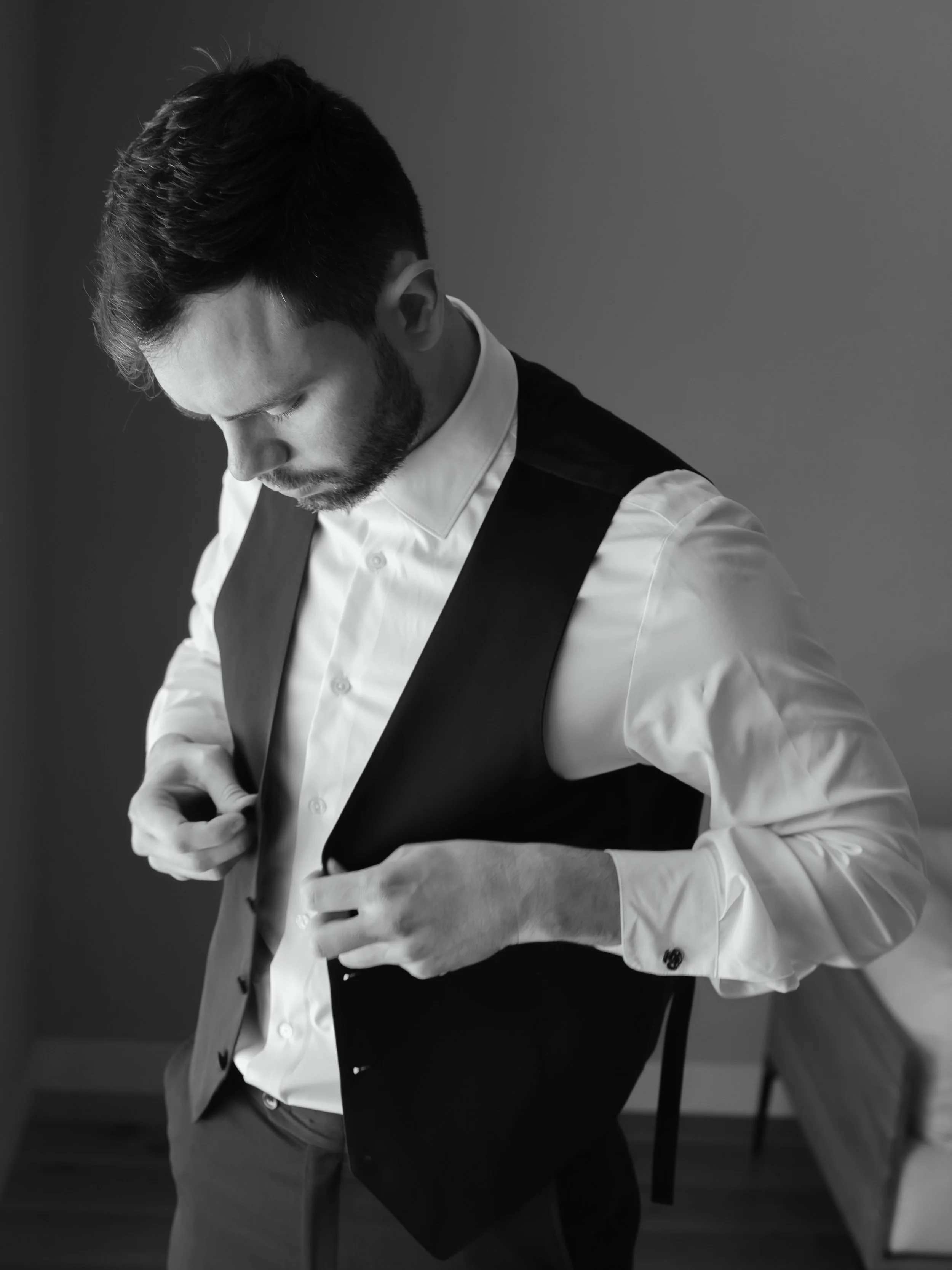 Black and white portrait of groom buttoning his vest during getting ready moments before an Ohio wedding ceremony.