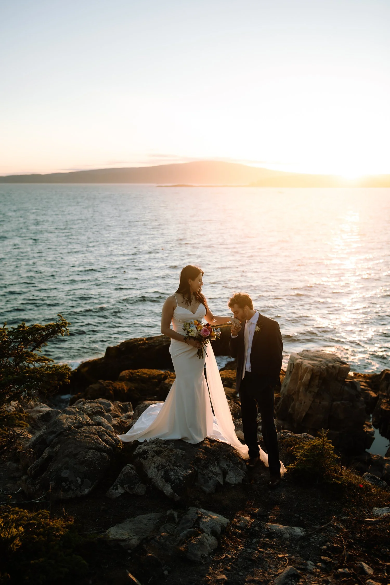 Bride and groom standing together on coastal cliffs at sunset during an Acadia National Park elopement