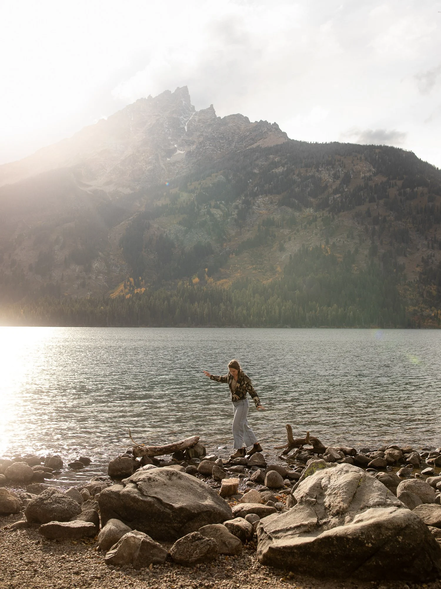 Person standing along the rocky shoreline of Jenny Lake beneath the Tetons