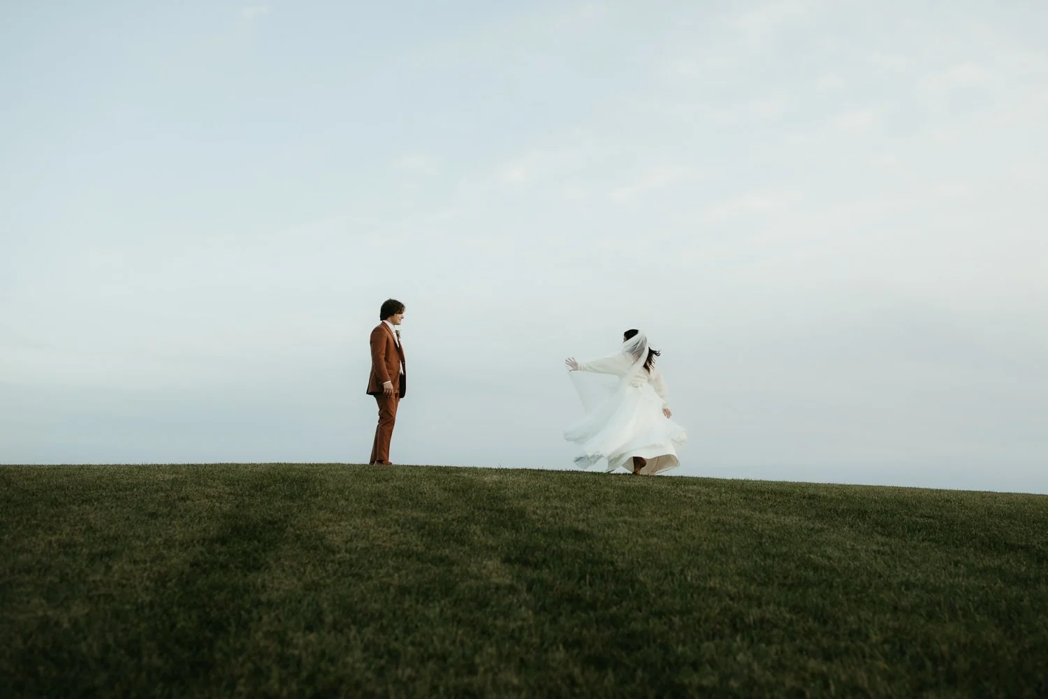 Bride and groom have their first look moment on a grassy hilltop at Ivory Meadows wedding venue, with a vast sky backdrop.
