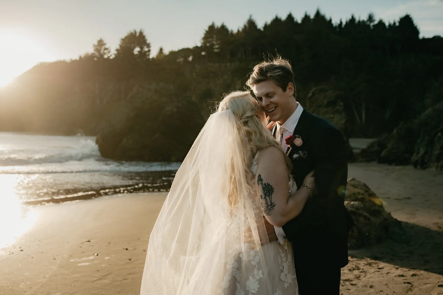 Bride and groom laughing together on the beach at sunset