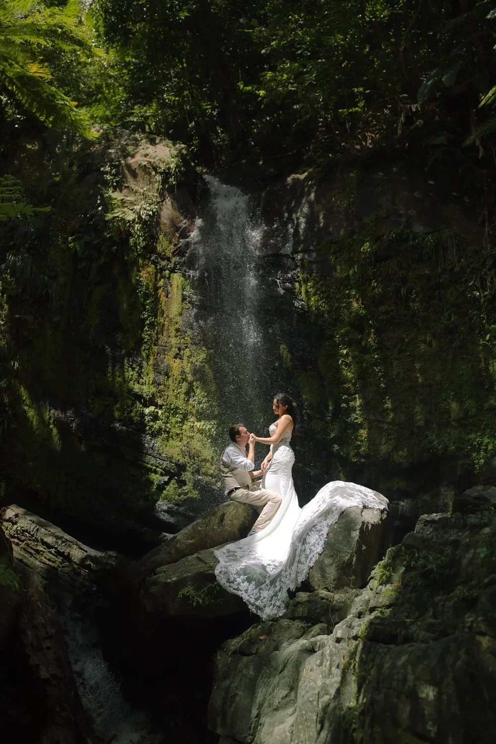 Romantic elopement portrait of a couple by a waterfall in El Yunque rainforest, surrounded by lush tropical foliage.