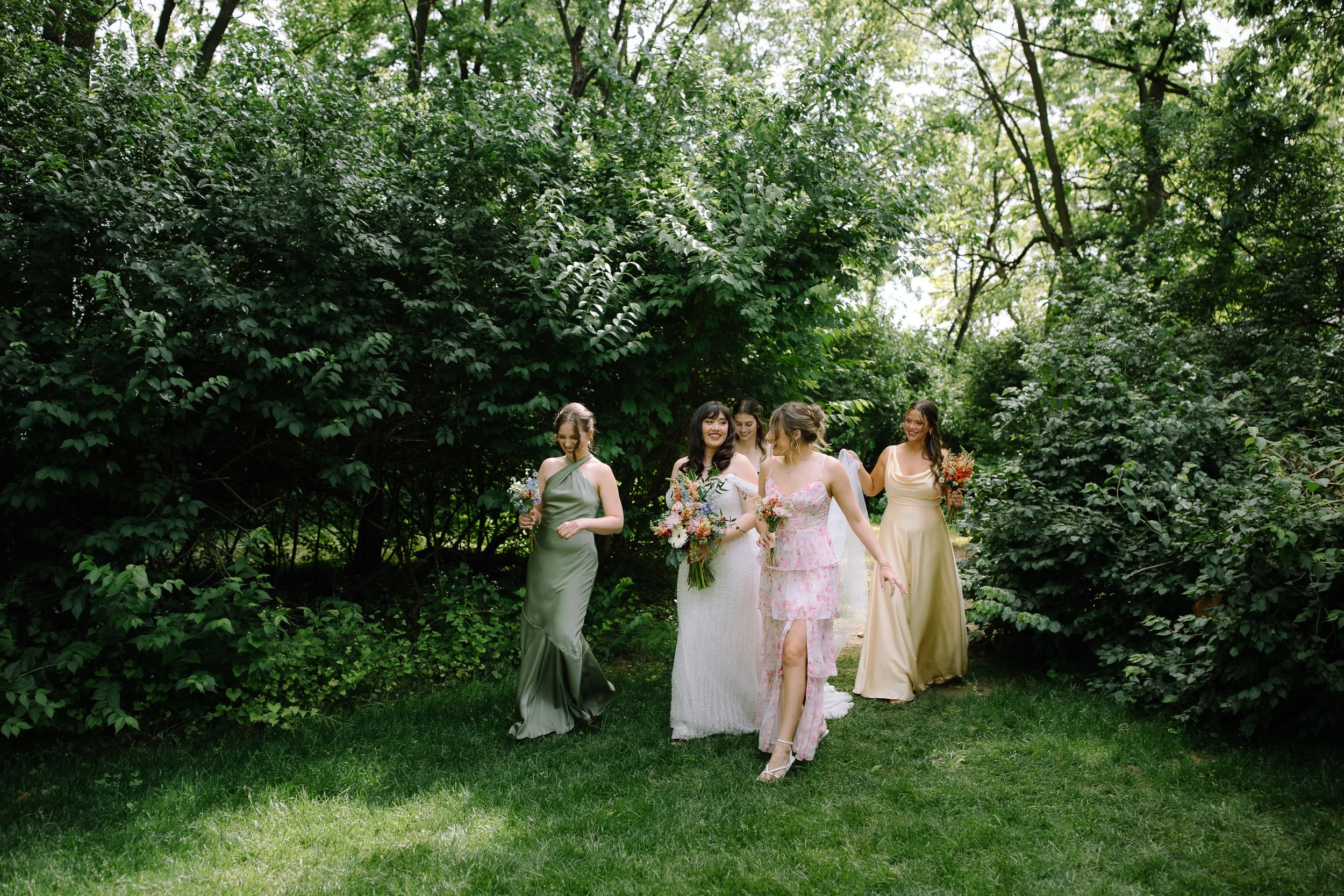 Bride and bridesmaids walking together through a lush garden during wedding party portraits.