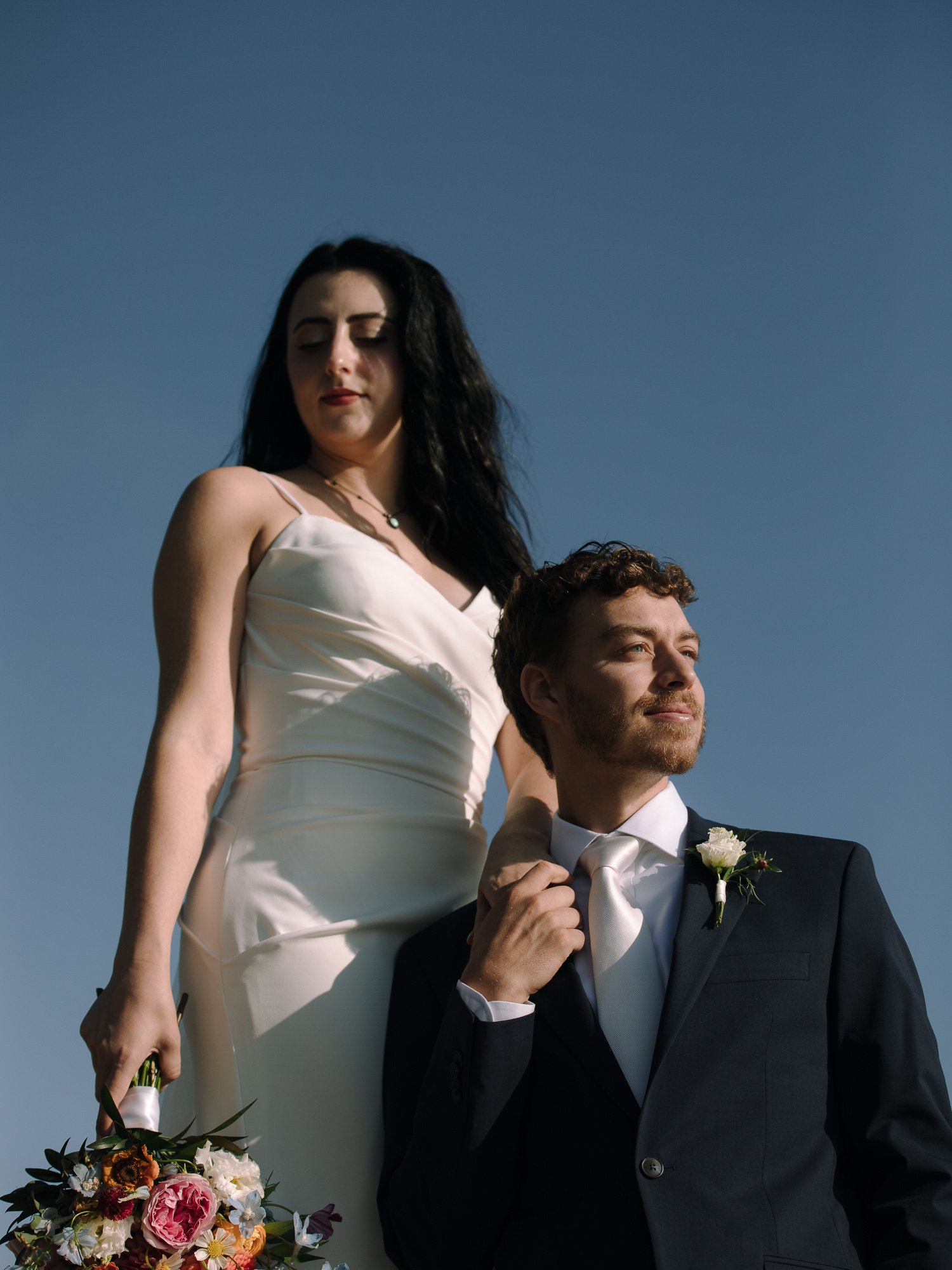Bride and groom standing together on rocky coastline during an Acadia National Park elopement with clear morning sky