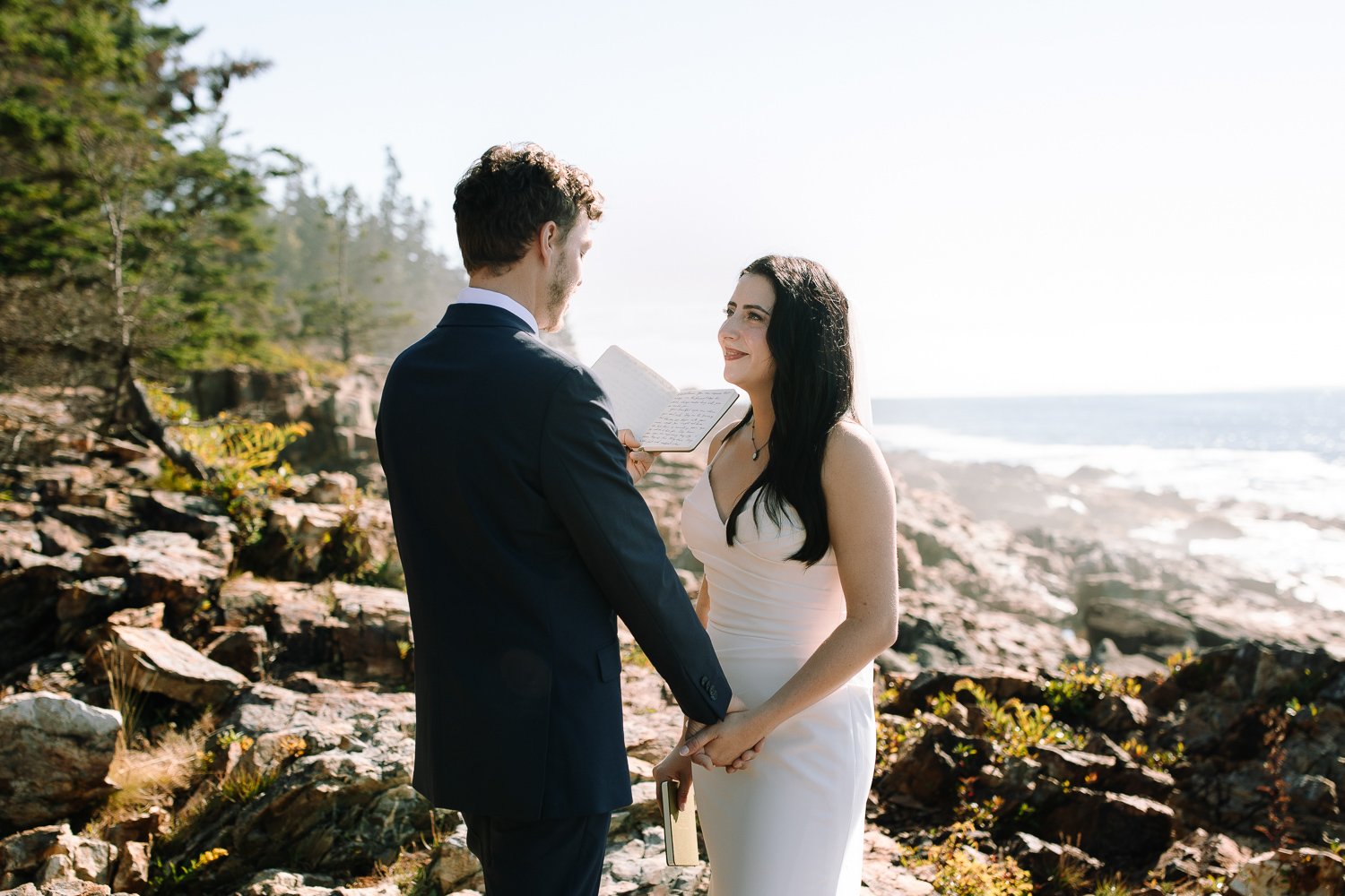 Bride and groom holding hands and reading vows during an intimate Acadia elopement ceremony by the ocean