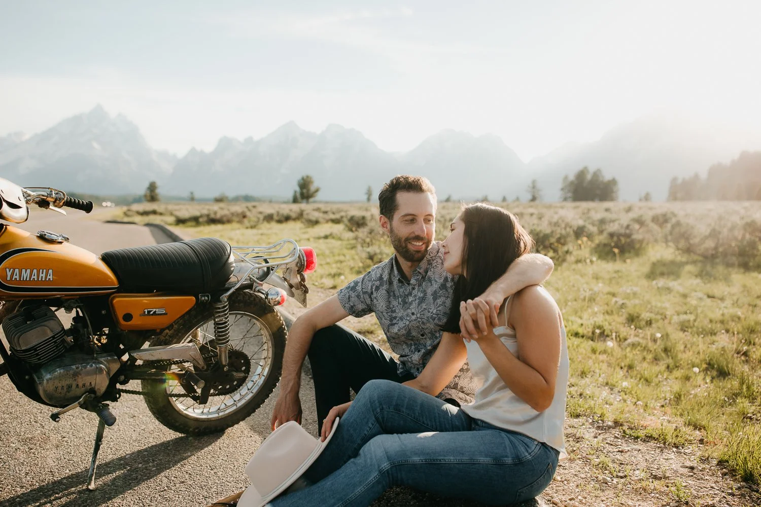 Couple sitting together beside a vintage motorcycle during a Grand Teton engagement session
