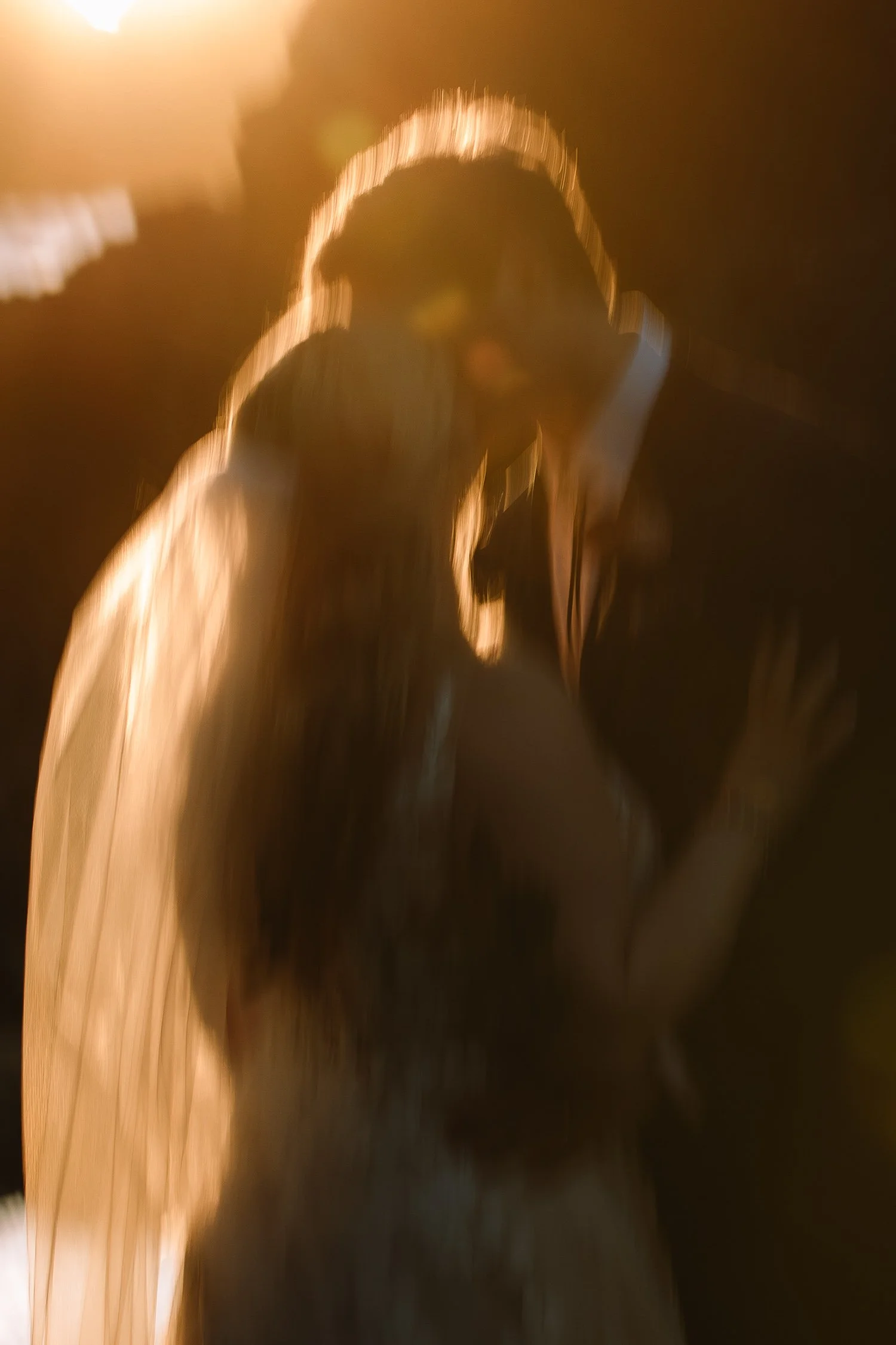 Soft motion blur kiss between bride and groom during golden hour