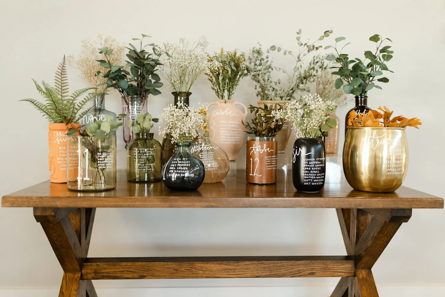 Creative escort card seating chart display with handwritten names and greenery for an Ivory Meadows wedding in Dayton, Ohio