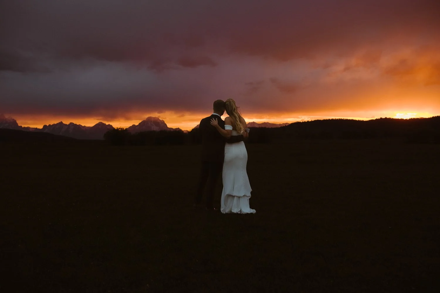 Couple embracing during a dramatic sunset elopement in Grand Teton National Park with colorful storm clouds overhead.