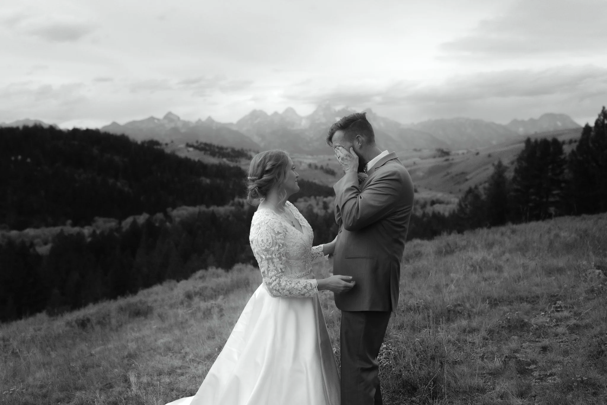 Black and white image of a bride comforting groom during an emotional moment in the mountains