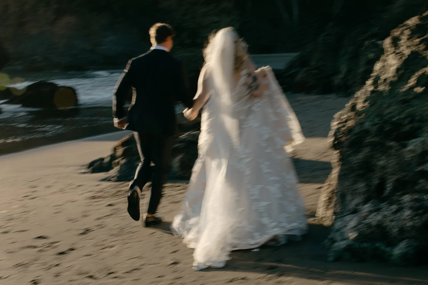 Newlyweds running hand in hand across the sand at sunset at College Cove