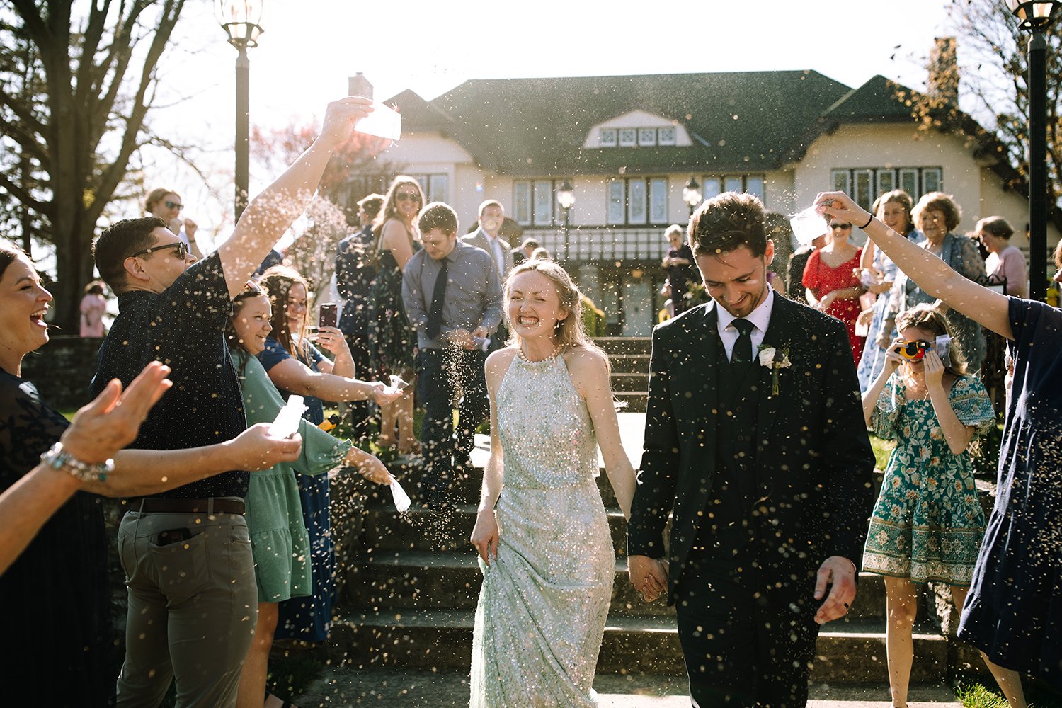 Bride and groom walk through guests during a joyful wedding exit at Orrmont Estate near Dayton, Ohio, with the historic estate in the background.