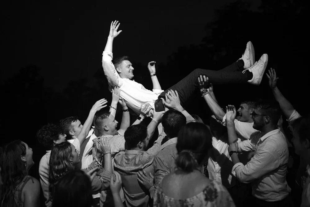 Groom lifted by friends on the dance floor during energetic wedding reception celebration.