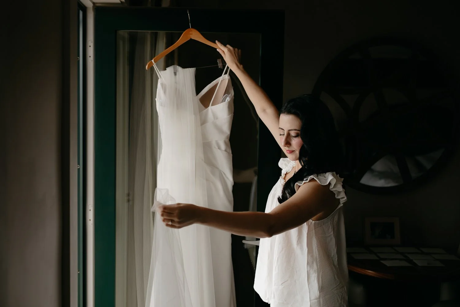 Bride holding her wedding dress in soft window light while getting ready for an Acadia National Park elopement.