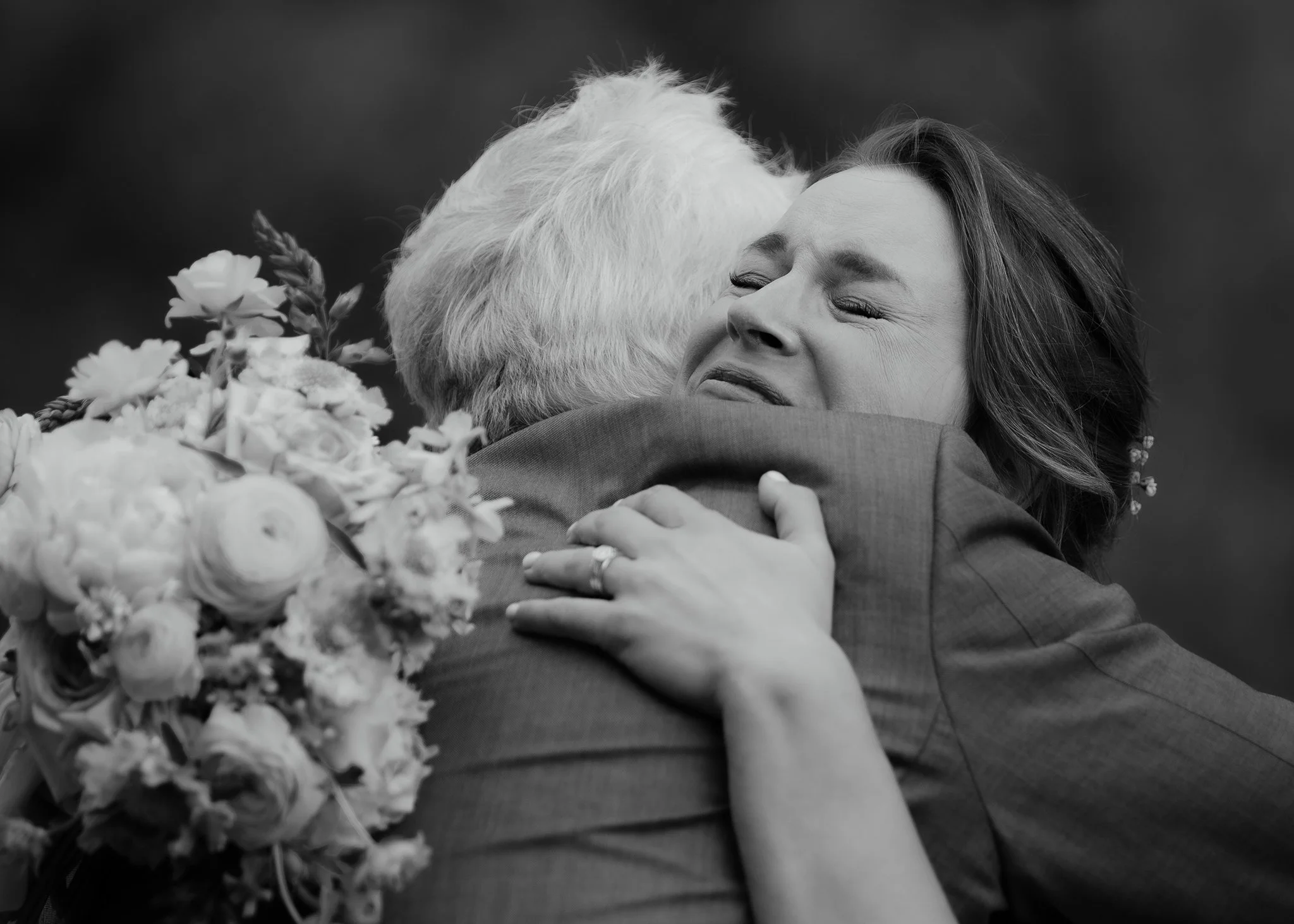 Emotional candid wedding photo of bride hugging family member, black and white meaningful wedding moment