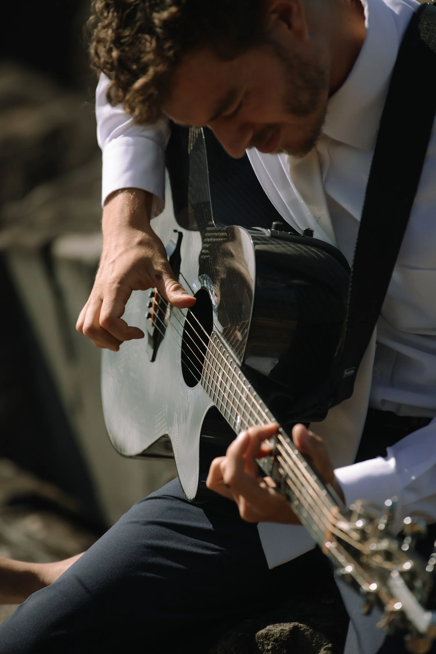 Groom playing guitar during an intimate Acadia National Park elopement, seated on coastal rocks by the ocean