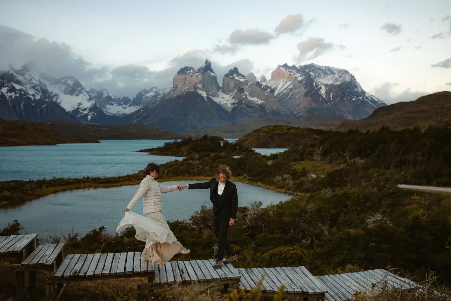 Couple holding hands on a boardwalk with mountain peaks and lake during a Patagonia elopement