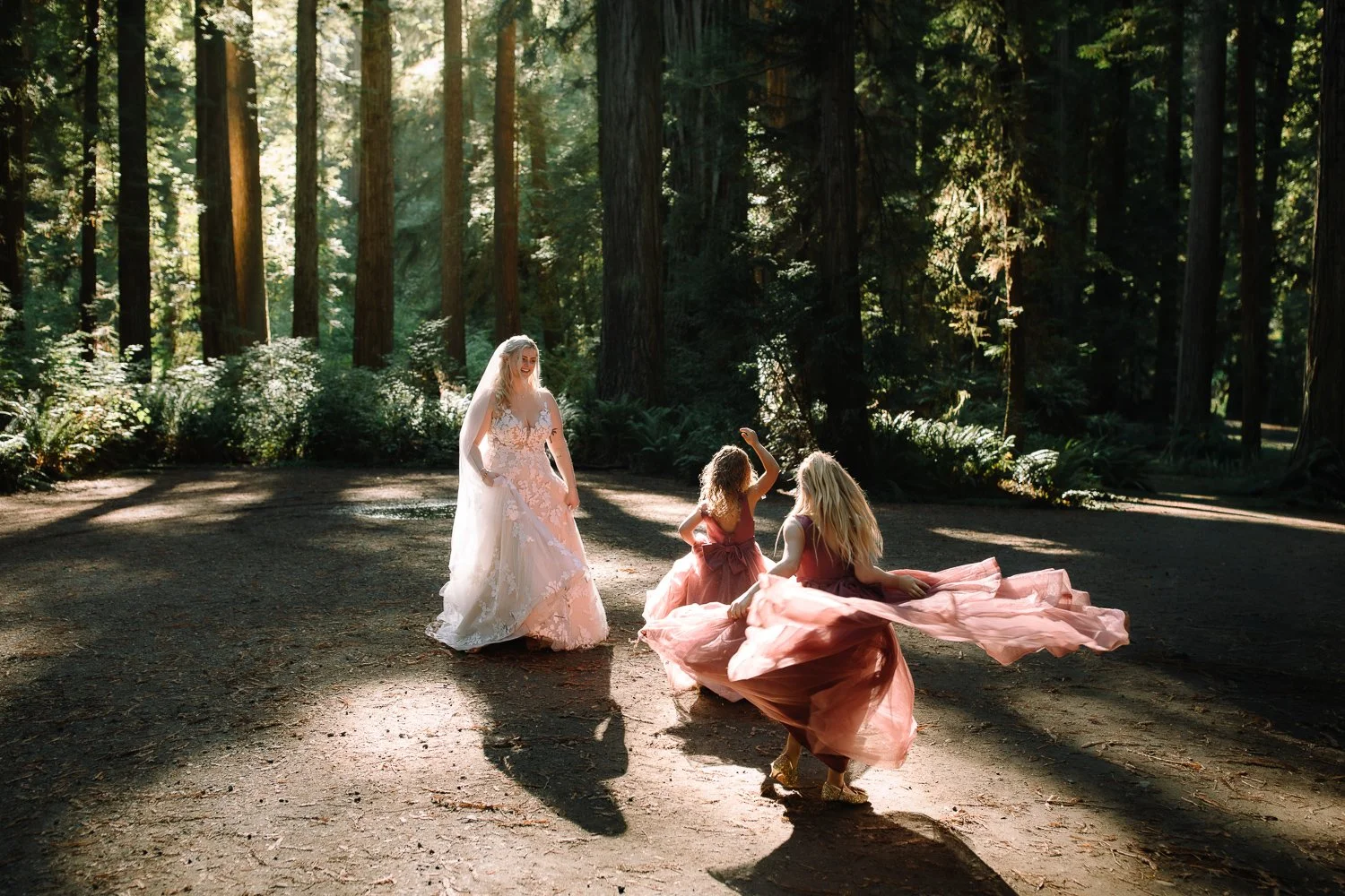 Bride and bridesmaids twirling in soft light inside a redwood forest