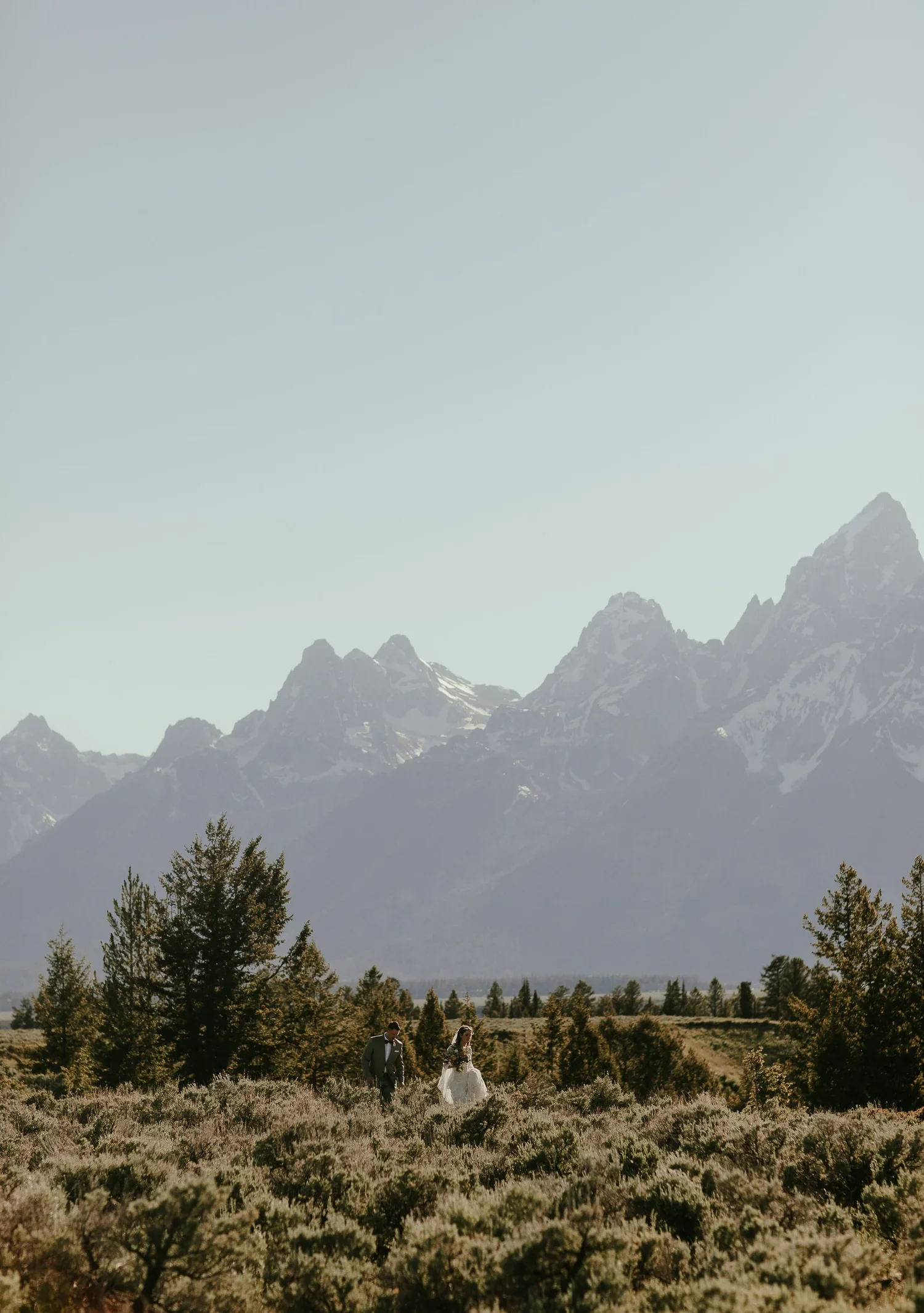 Bride and groom walking together in a wide open field with the Grand Teton Mountains in the background
