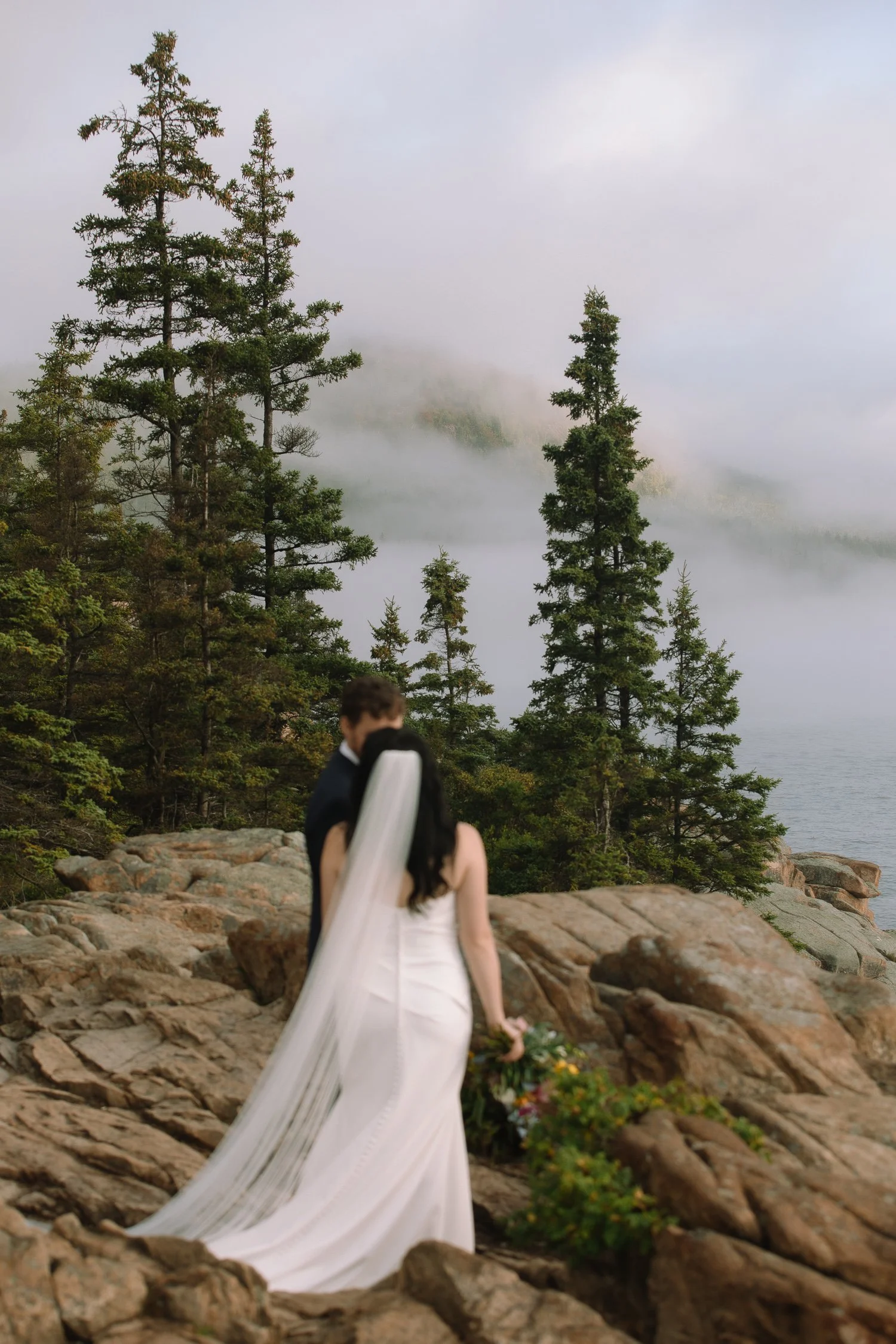 Bride walking across rocky cliffs during an early morning Acadia National Park elopement along the Maine coast.