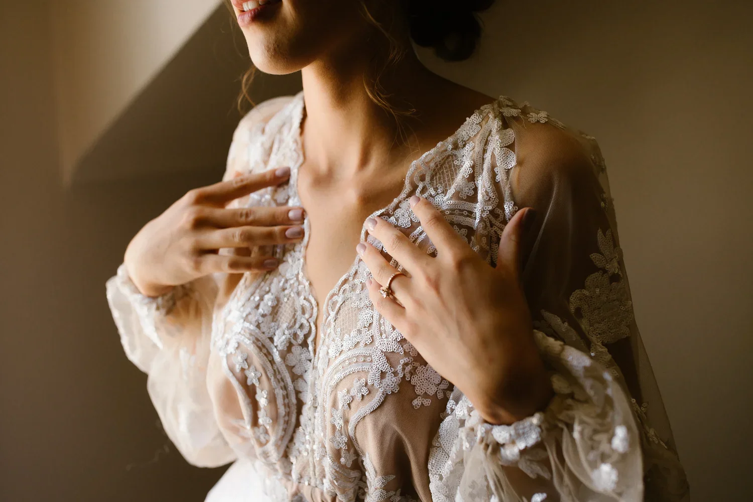 Close-up of bride adjusting lace wedding gown in soft window light during morning preparations