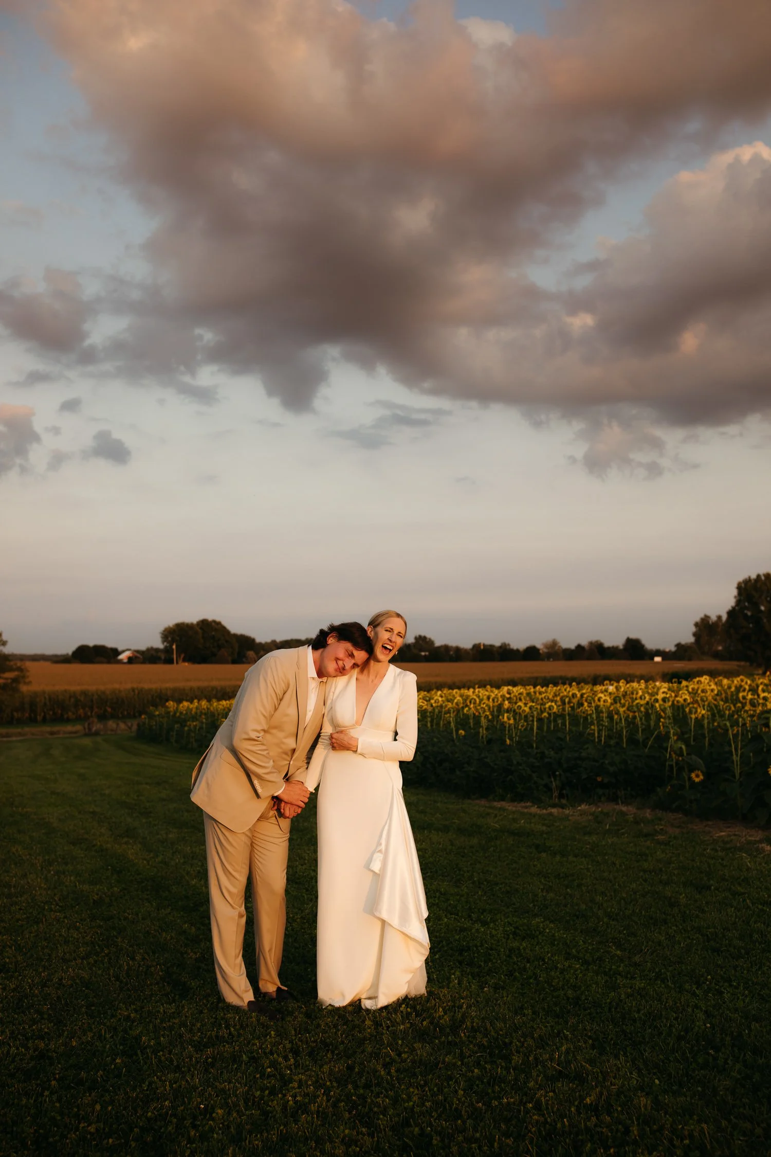Bride and groom laughing together during golden hour outdoor wedding portrait in open field